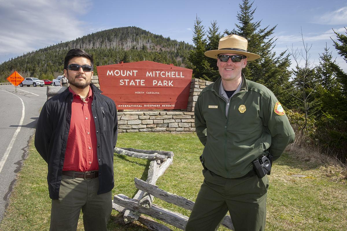 Young student and older alumni in uniform standing in front of a national park sign
