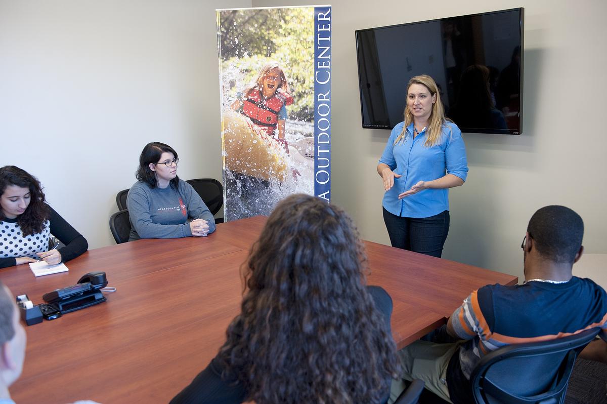 Woman standing at the front of a conference table with a display case behind her