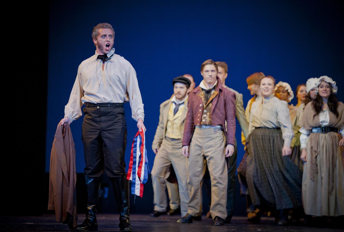 Students performing Les Miserables in front of an audience, solo singer performing center stage