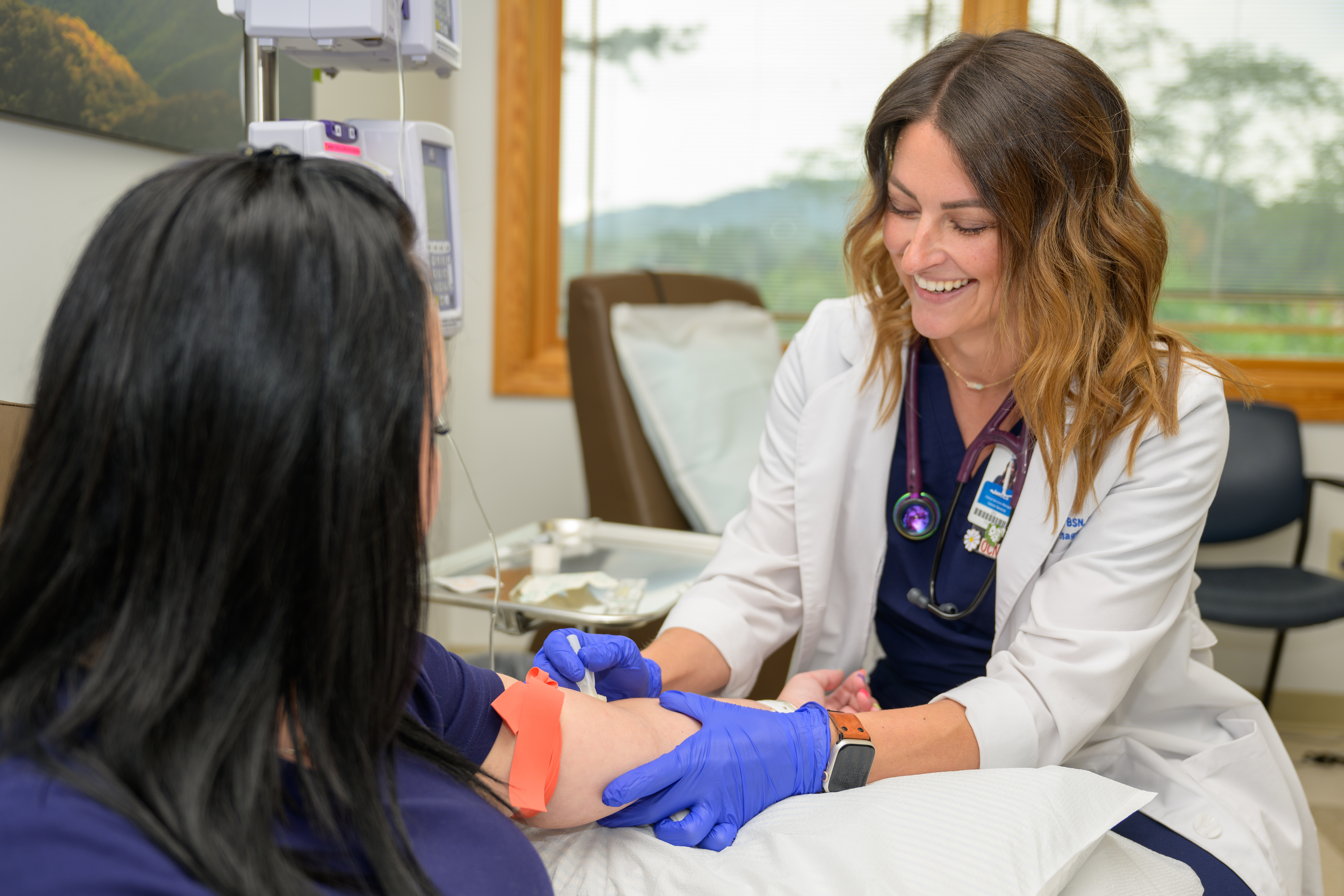 Female healthcare provider in white coat and blue gloves examines patient's arm in medical office.