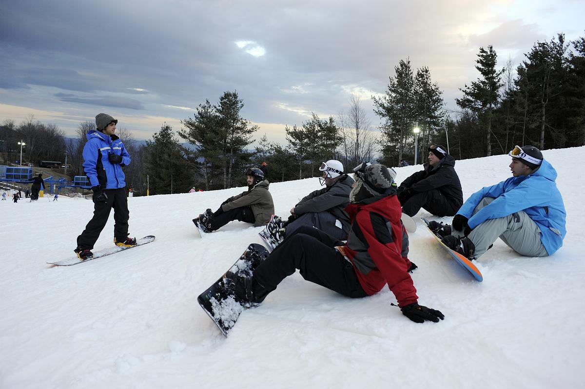Snowboarding instructor teaching students at the base of a slope