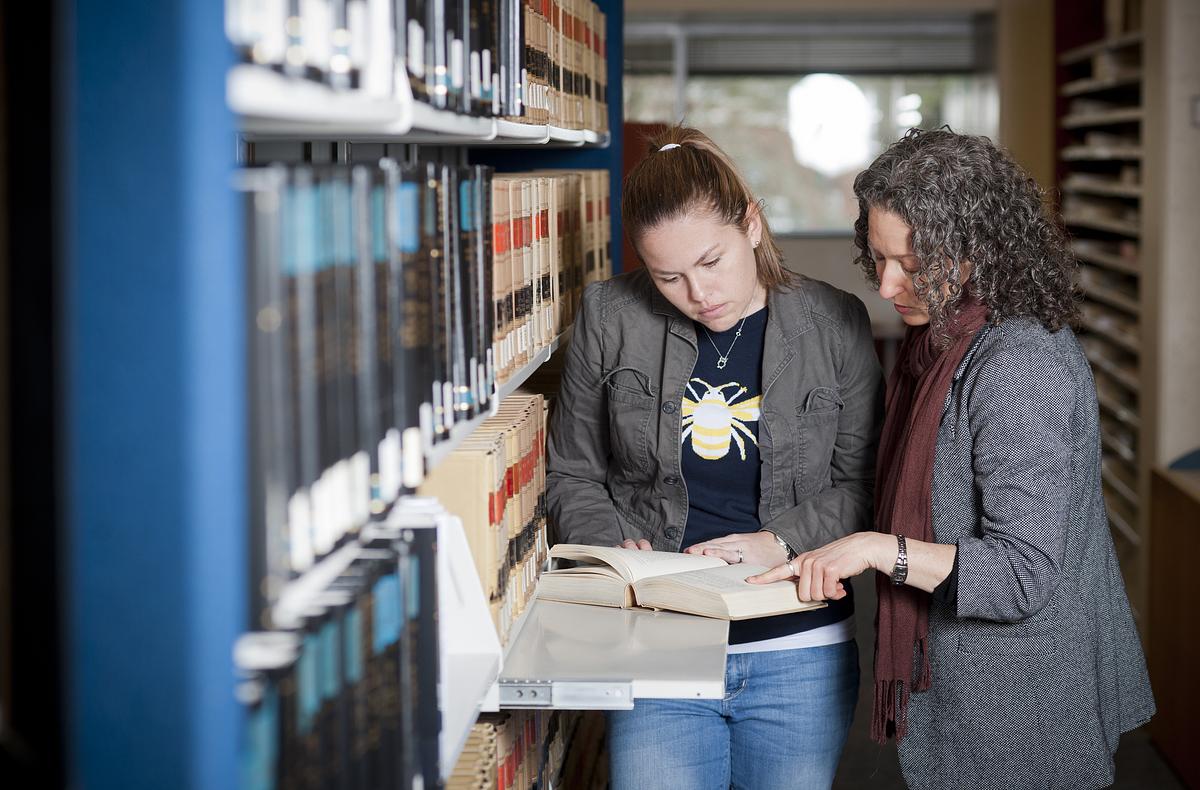 A teacher and student in a library looking over a book together