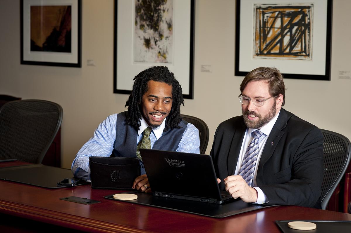 Young black student in a suit talking with older white man in a suit at a conference table