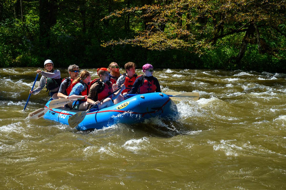 Students and guide rafting down a river through turbulent water