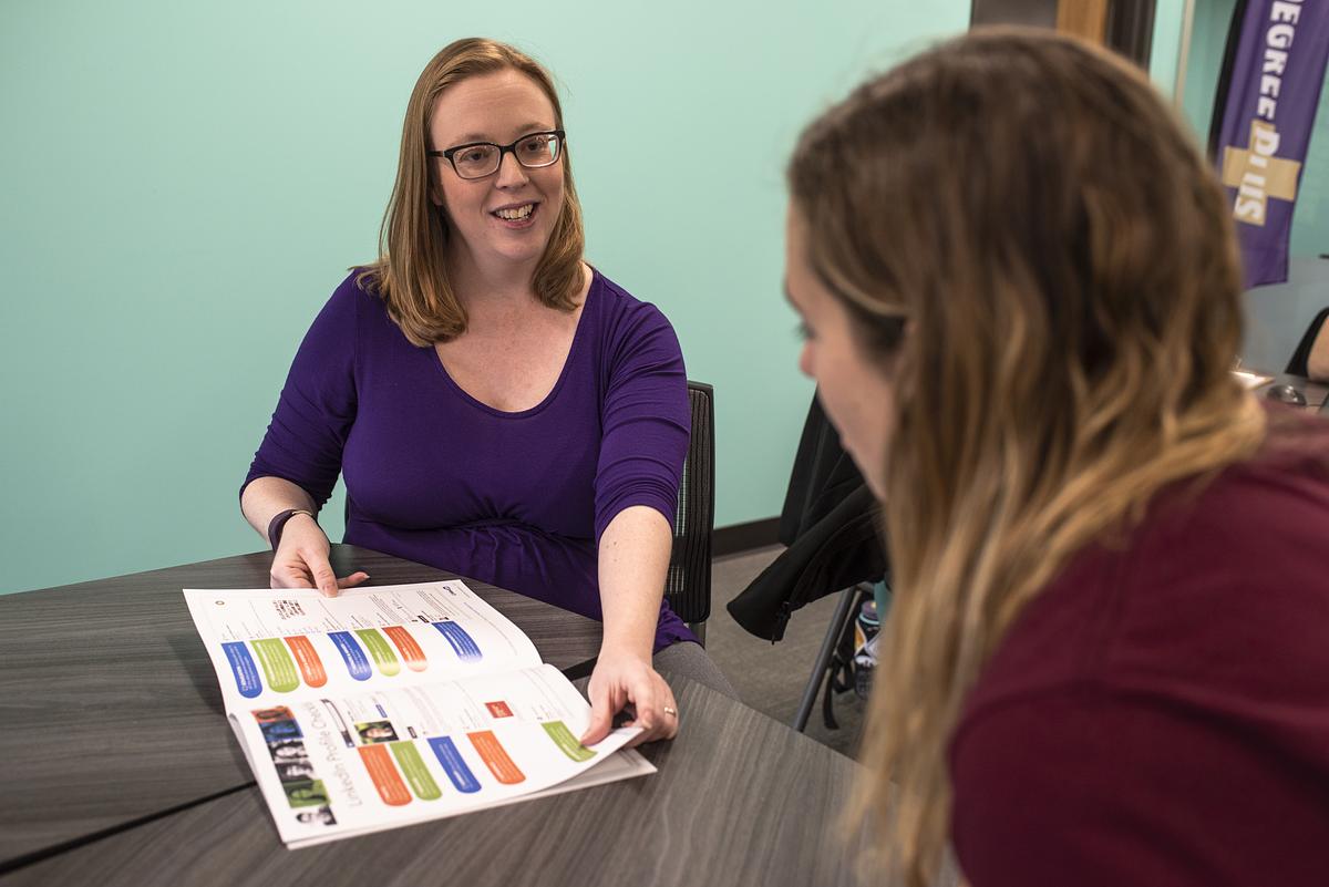 Picture of smiling woman showing a booklet to a student at a table