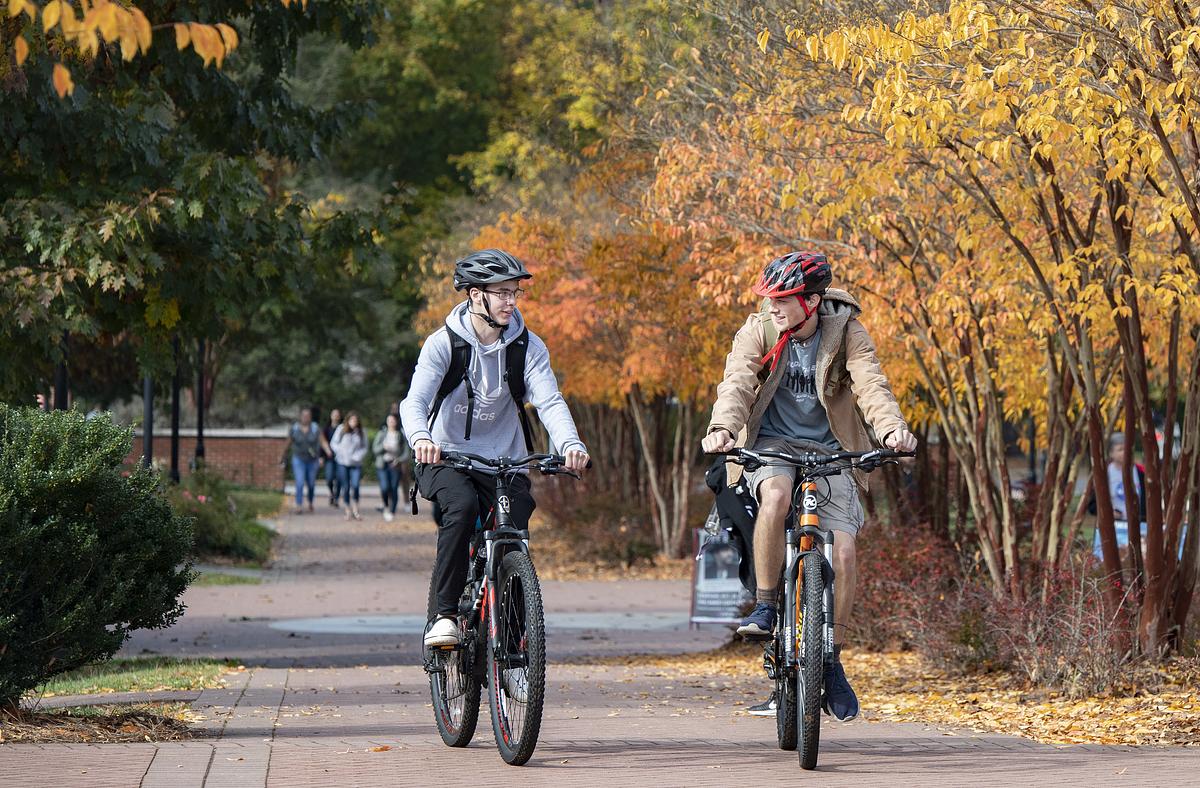 Two students riding bikes together on campus in the fall