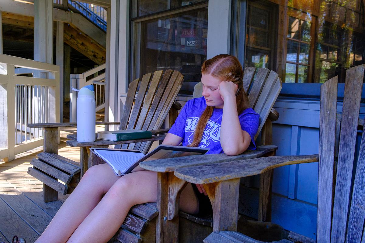 Student sitting in a wood chair on a porch reading
