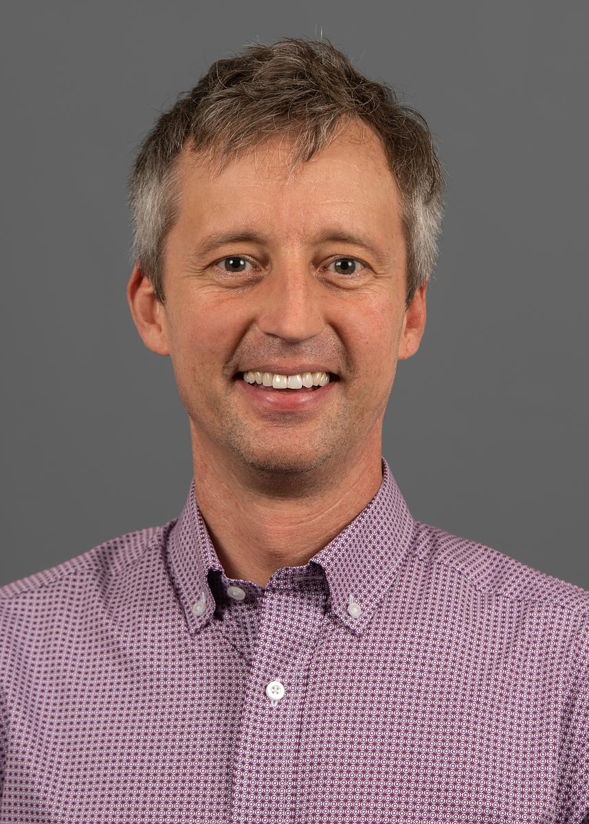 Darby Harris, a middle-aged man with gray hair smiling, wearing purple patterned button-up shirt against gray background