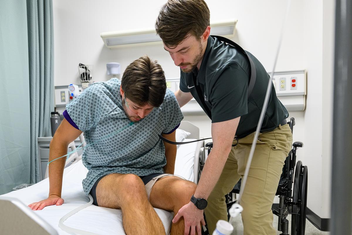 Physical therapist students helping up a patient from their hospital bed