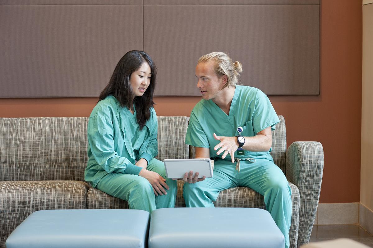 Two nursing students sitting on a couch and looking at a tablet together