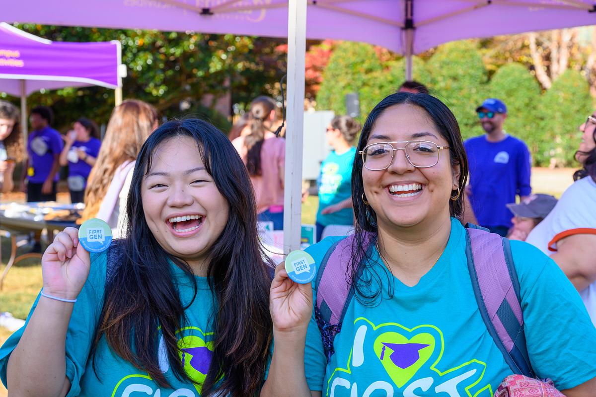 Two students smile with First Gen pins and I HEART FIRST GEN DAY t-shirts