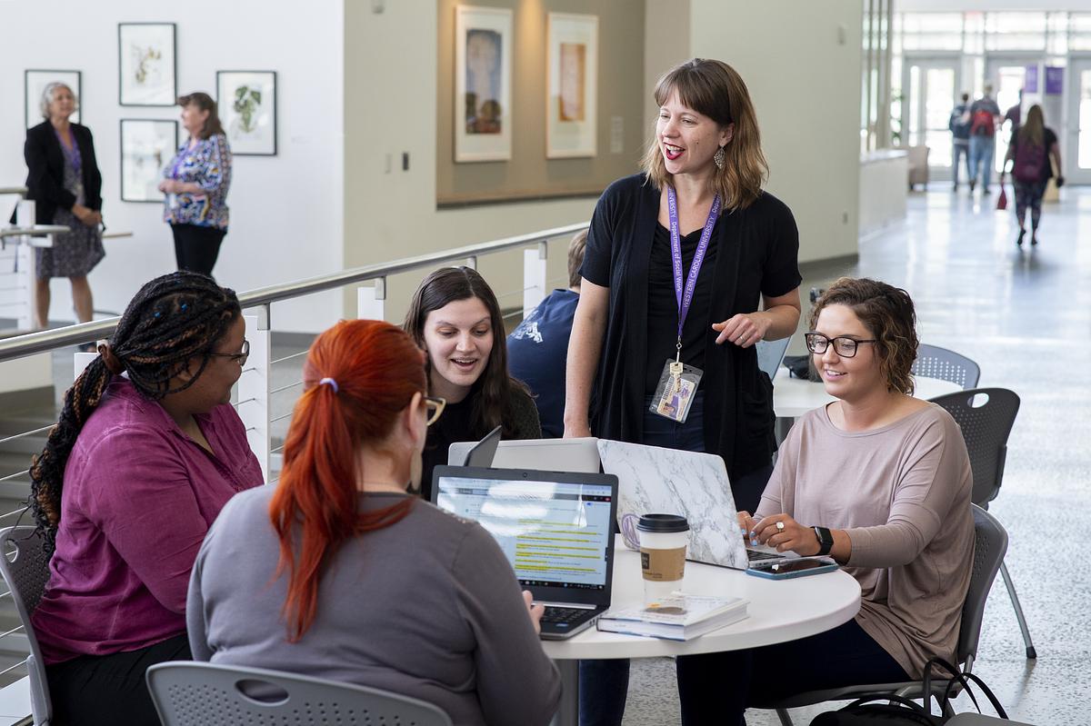 Teacher talking with students as they work together at a table with their laptops