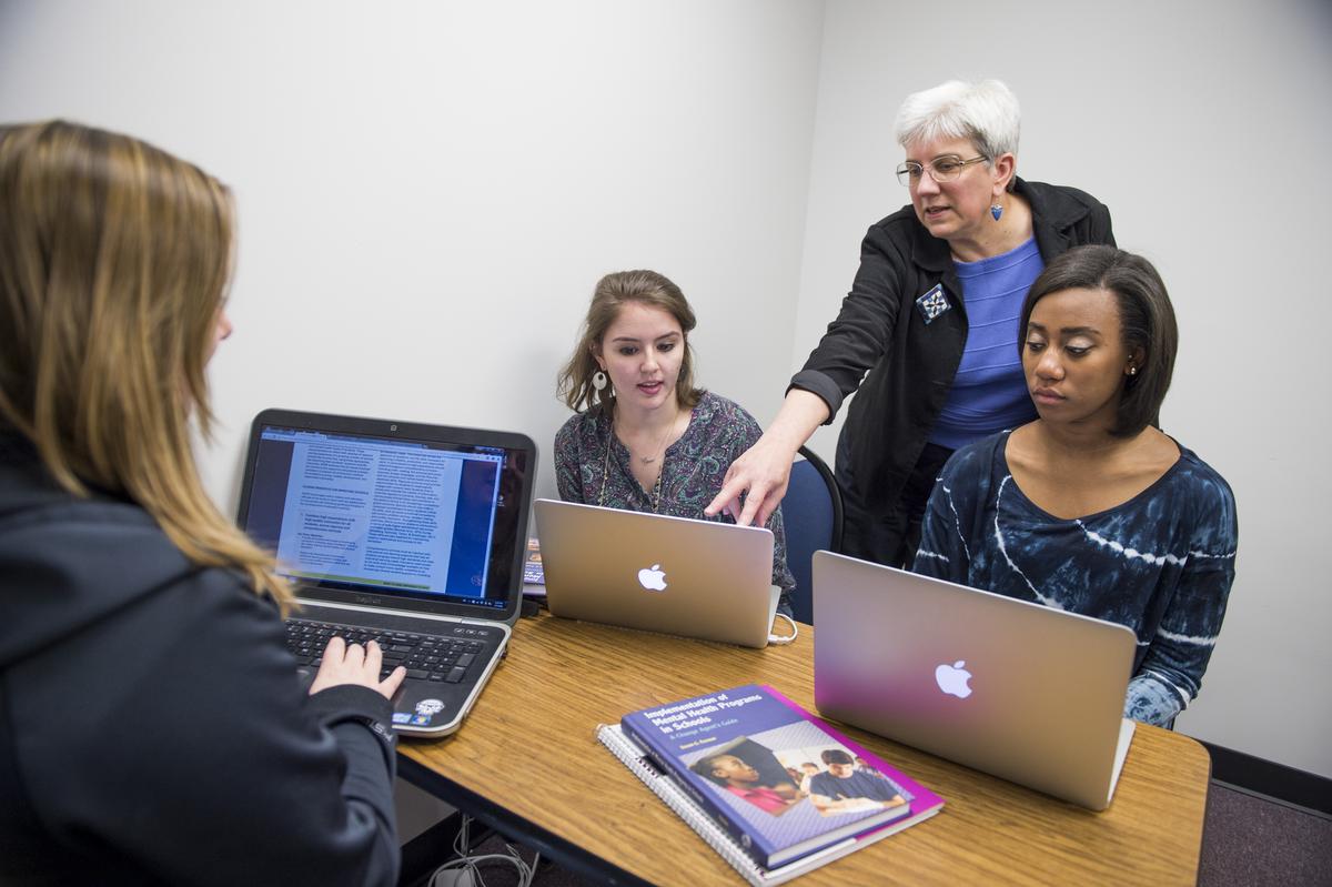 Students and faculty working together at a desk on laptops