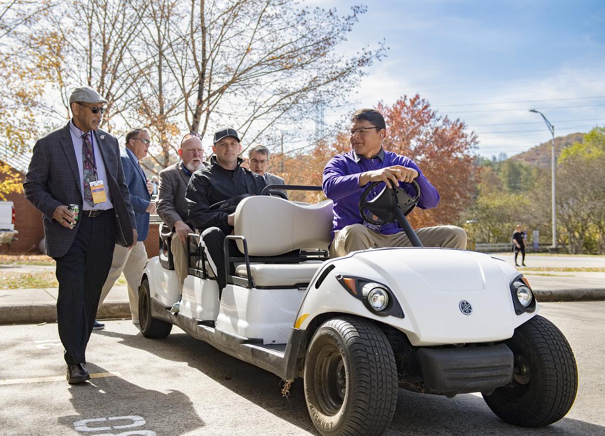 Student driving a golf cart with coaches in the passenger seats