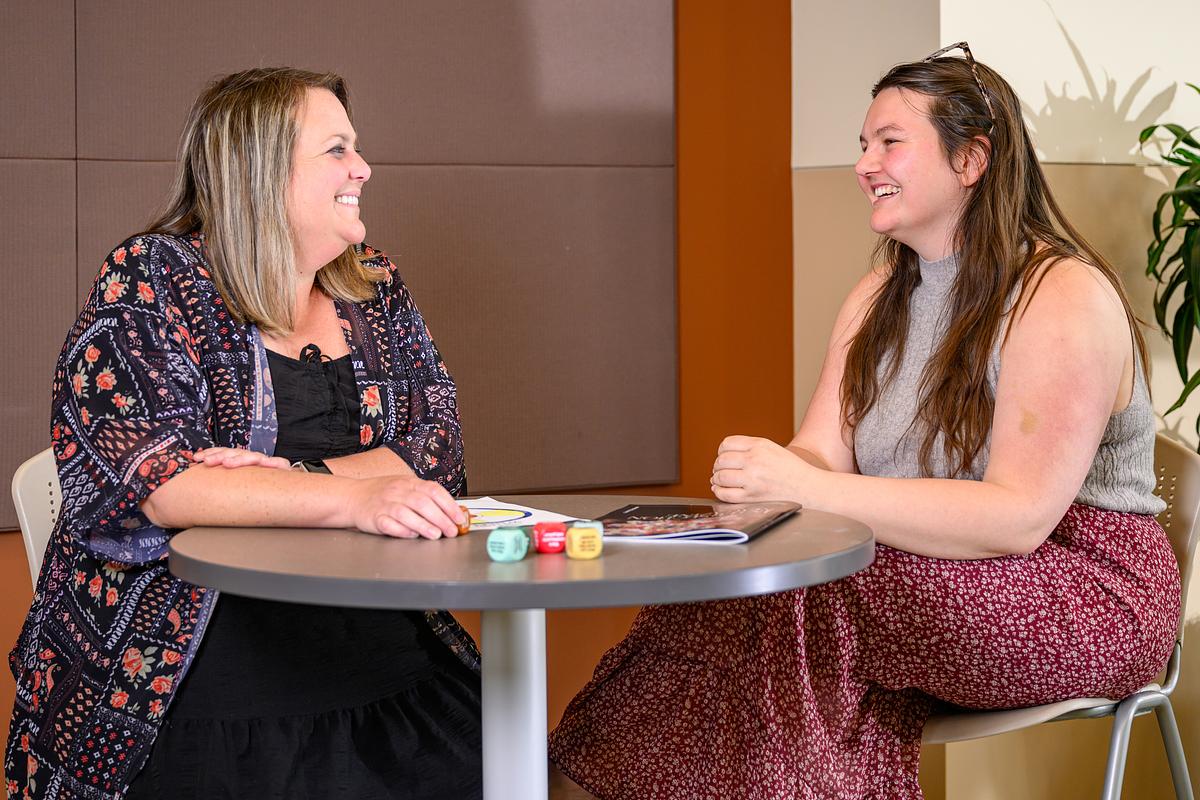 Masters in counseling student and teacher sit and talk around a table