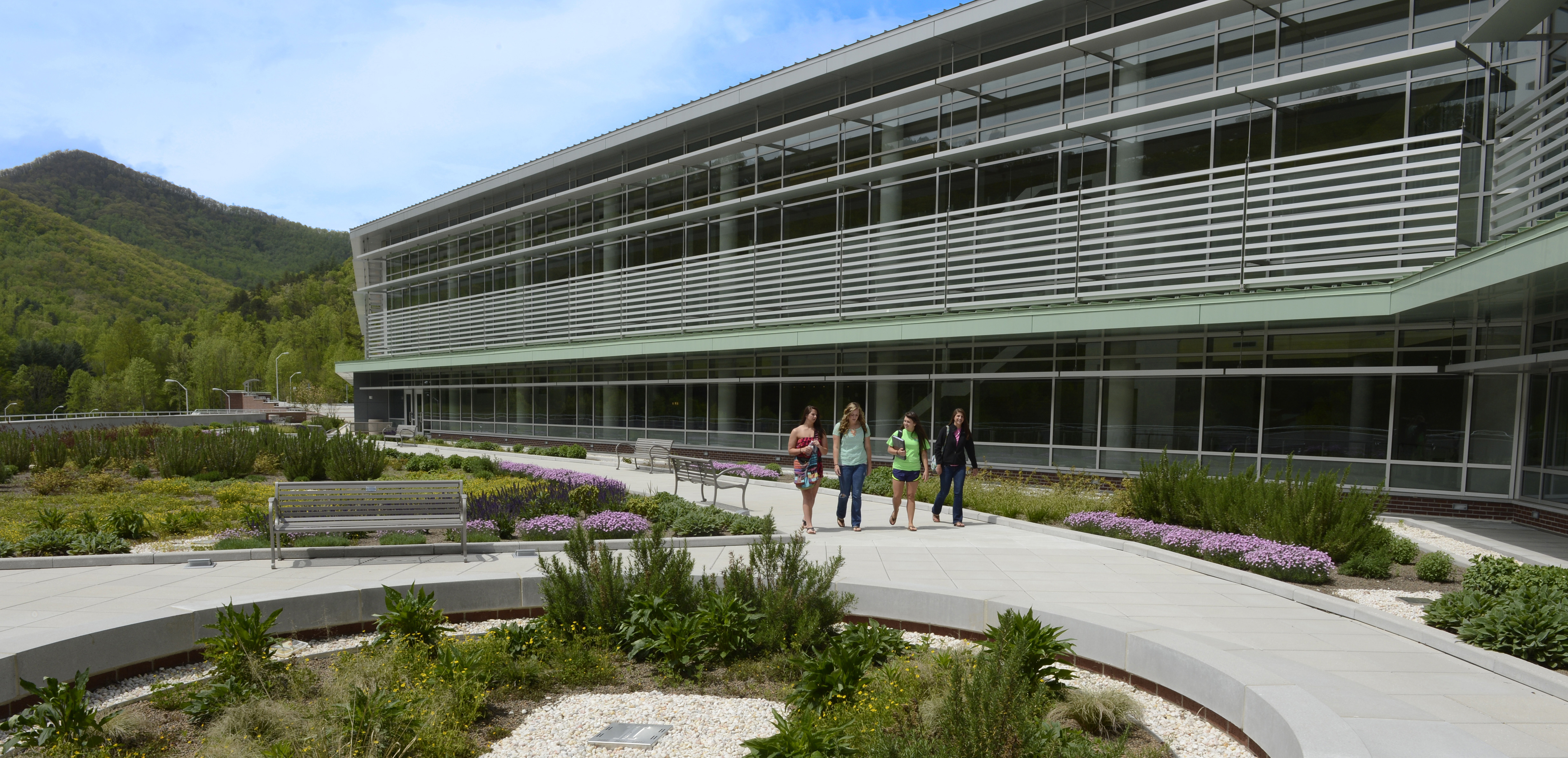 Exterior of the Health and Human Sciences Building surrounded by mountains on a sunny day with students walking out front