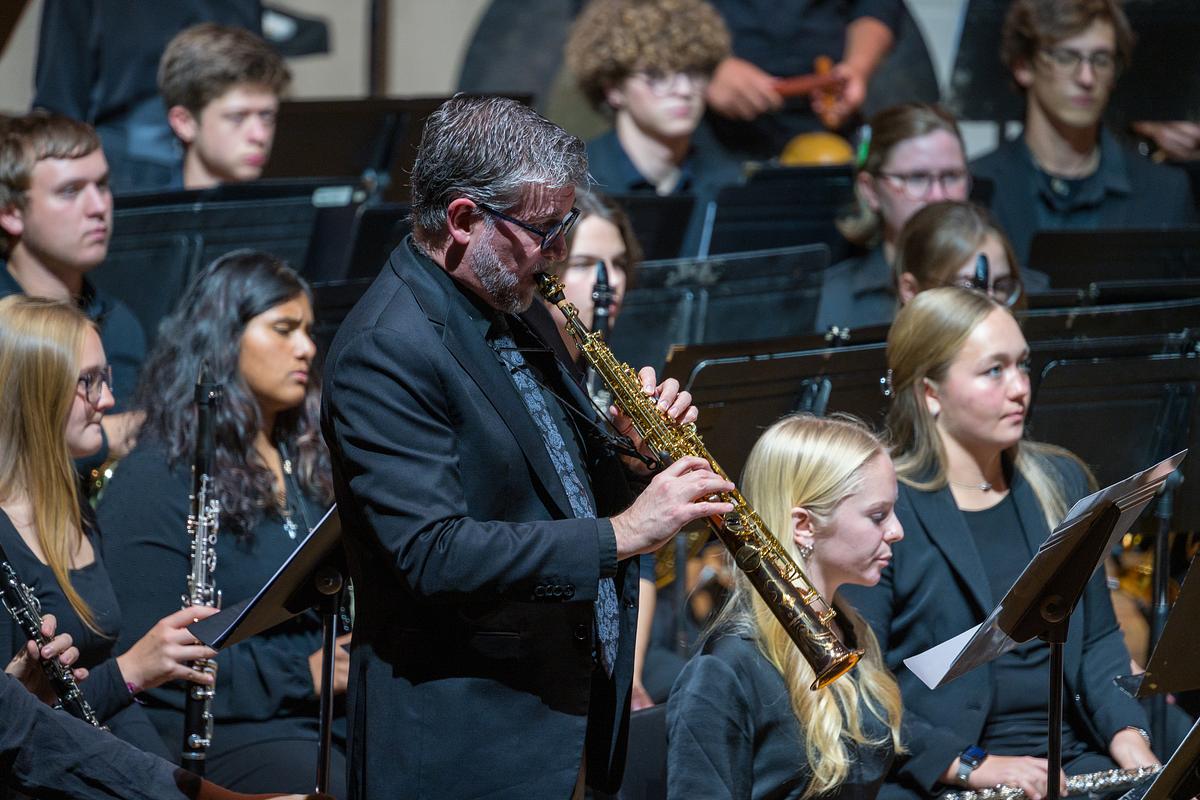 Professor playing an instrument on stage with students at the SOM Wind Ensemble