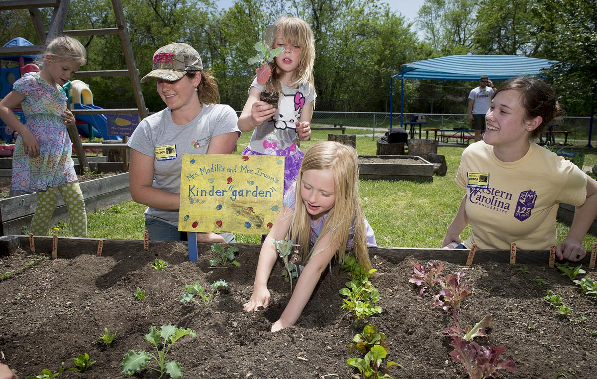 Student and children planting vegetables in a raised garden bed