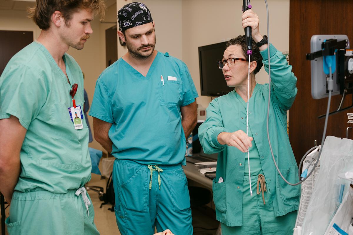 Three healthcare professionals in surgical attire examining medical equipment in a clinical setting.
