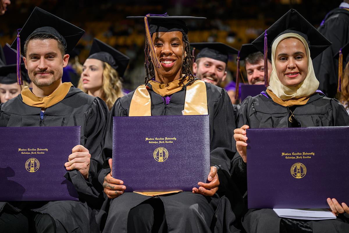 Students smiling and holding up their diplomas during commencement