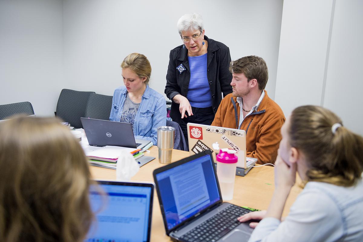 Professor teaching students around their laptops