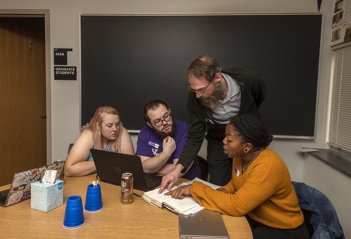 Professor mentors students working on various math problems at a table