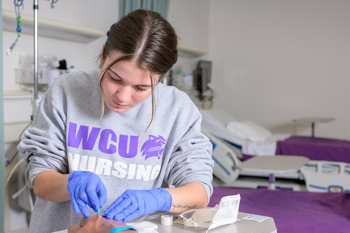 Young student wearing purple Ģ������ƵNursing shirt and blue gloves working in clinical laboratory setting.