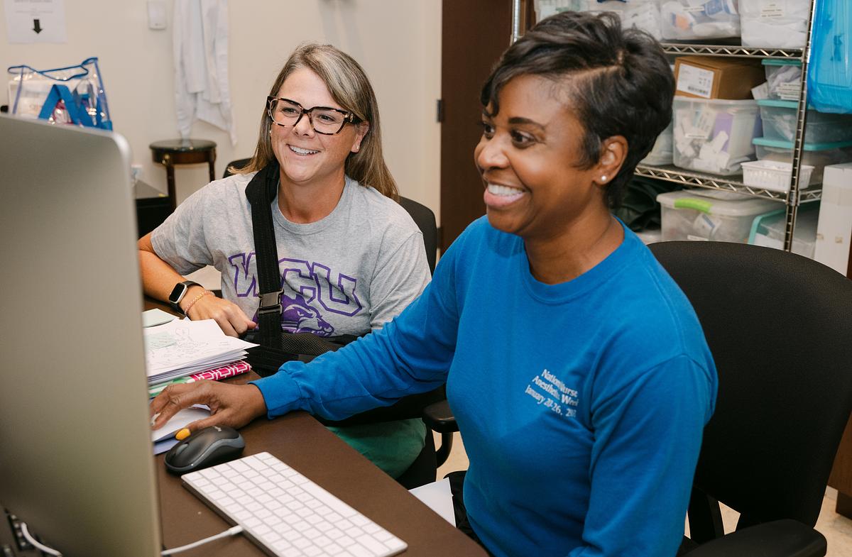 Nursing students sitting together at a desk smiling and working on a computer together