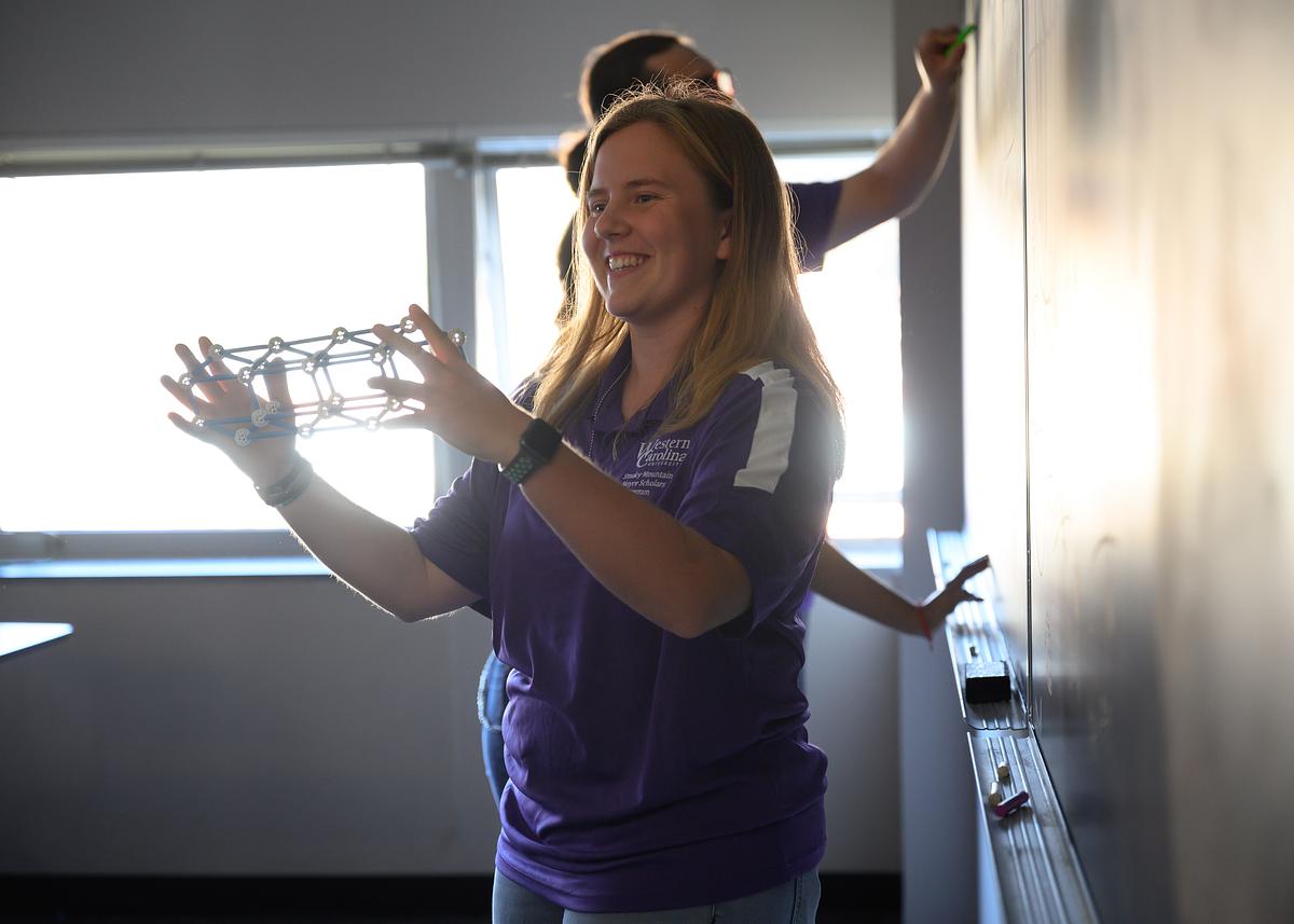 Noyce program member holding up an object in a classroom smiling
