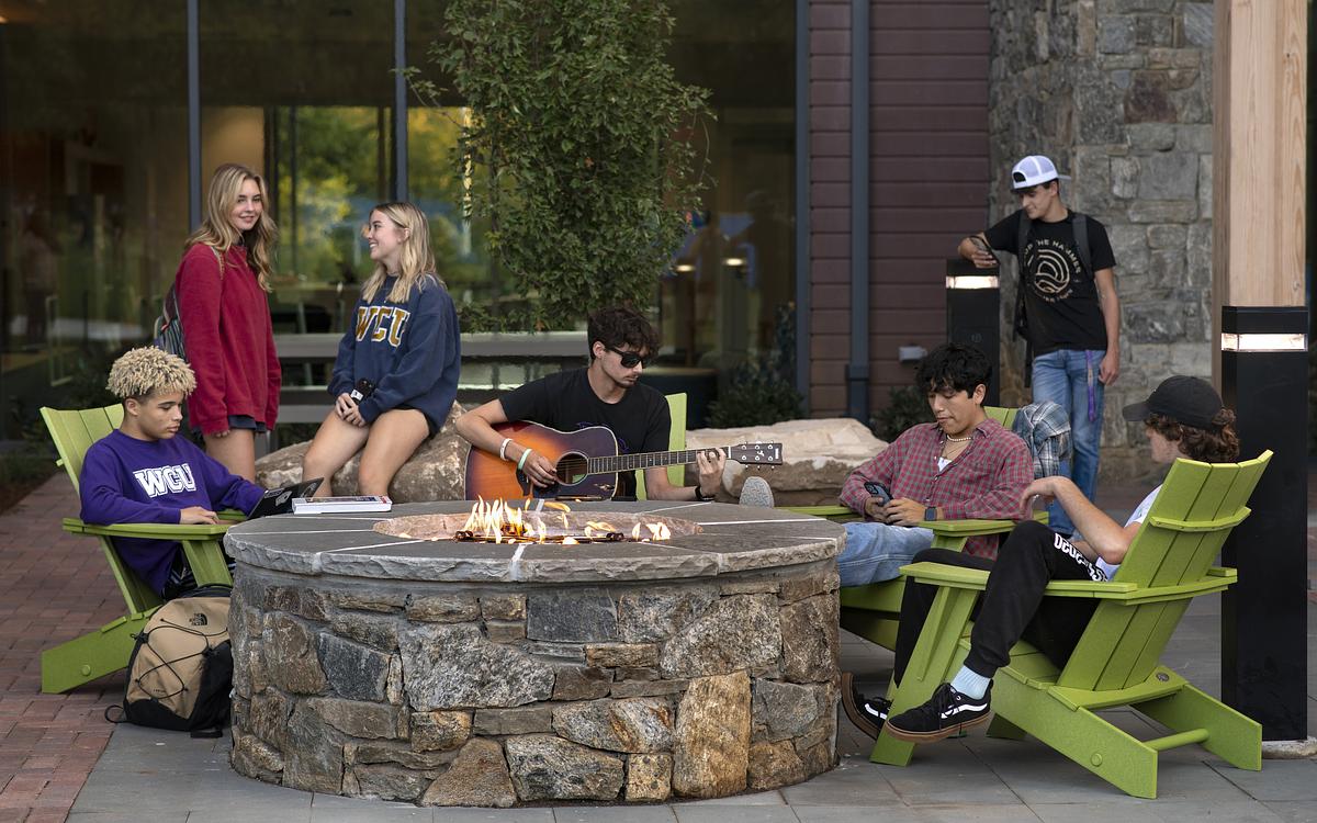 Students sitting in front of a fire pit at The Rocks Dorms playing music and relaxing 