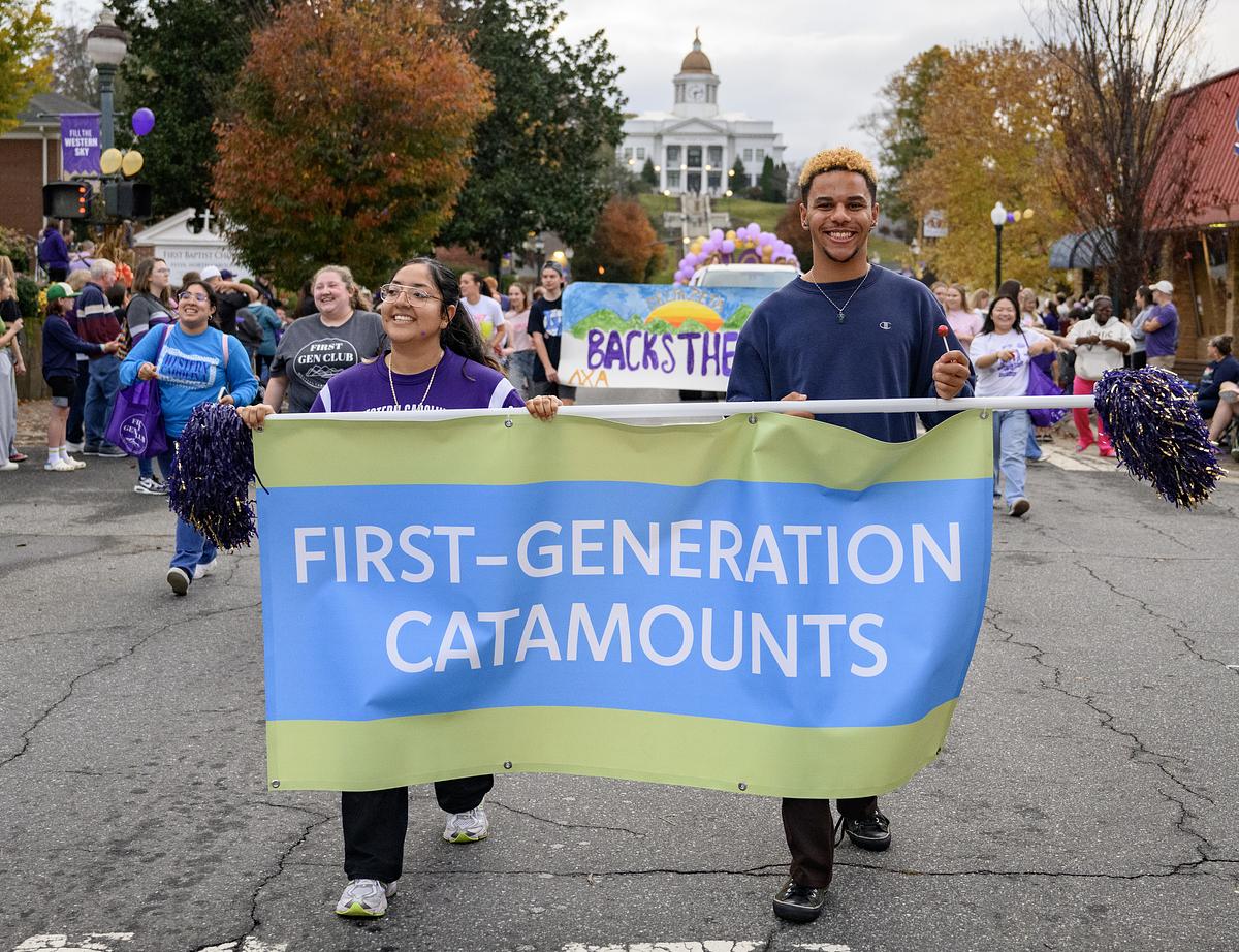Two students walking in Homecoming Parade carrying First Generation Catamounts banner in blue and teal