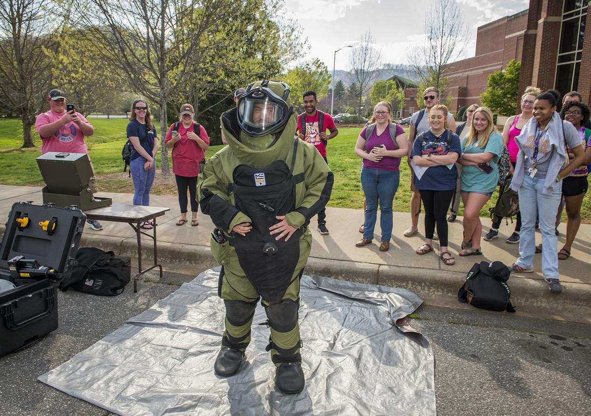 Individual wearing a protective bomb suit with a crowd gathered around for a demonstration