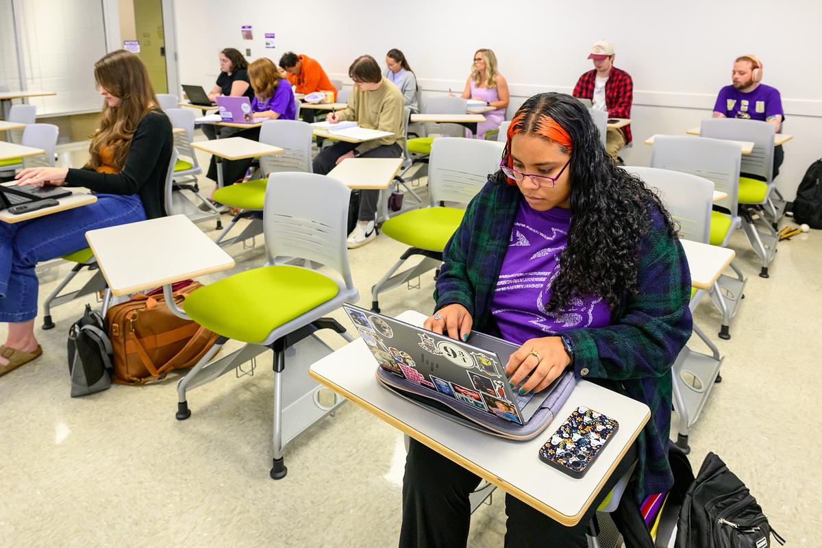Students sitting at desks in a classroom taking notes on their laptops