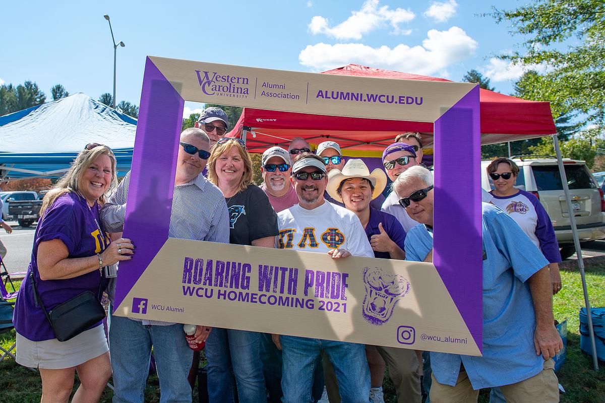 Alumni gathered together for a group photo holding a large frame