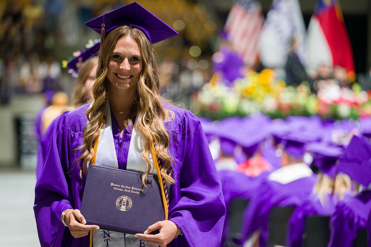 Student smiling and walking holding their diploma at commencement