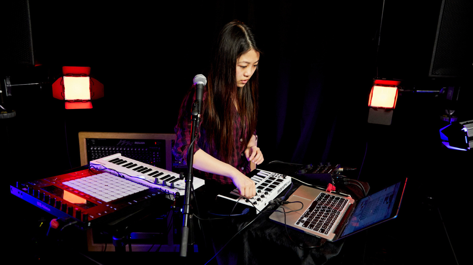A musician performs on electronic digital instruments in a dark studio